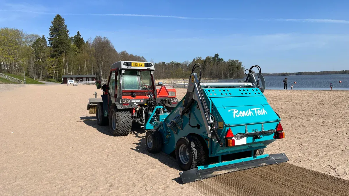 Tracteur avec accessoire BeachTech nettoyant une plage de lac avec du sable humide.