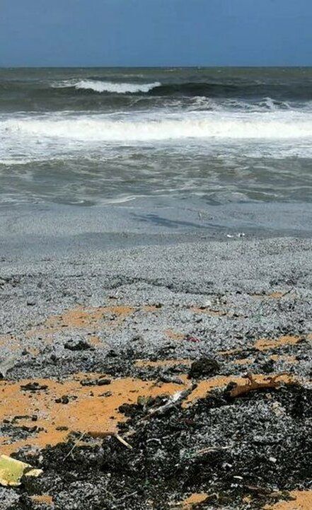 Granuli di plastica (nurdles) sulla spiaggia dello Sri Lanka, fumo nero sullo sfondo