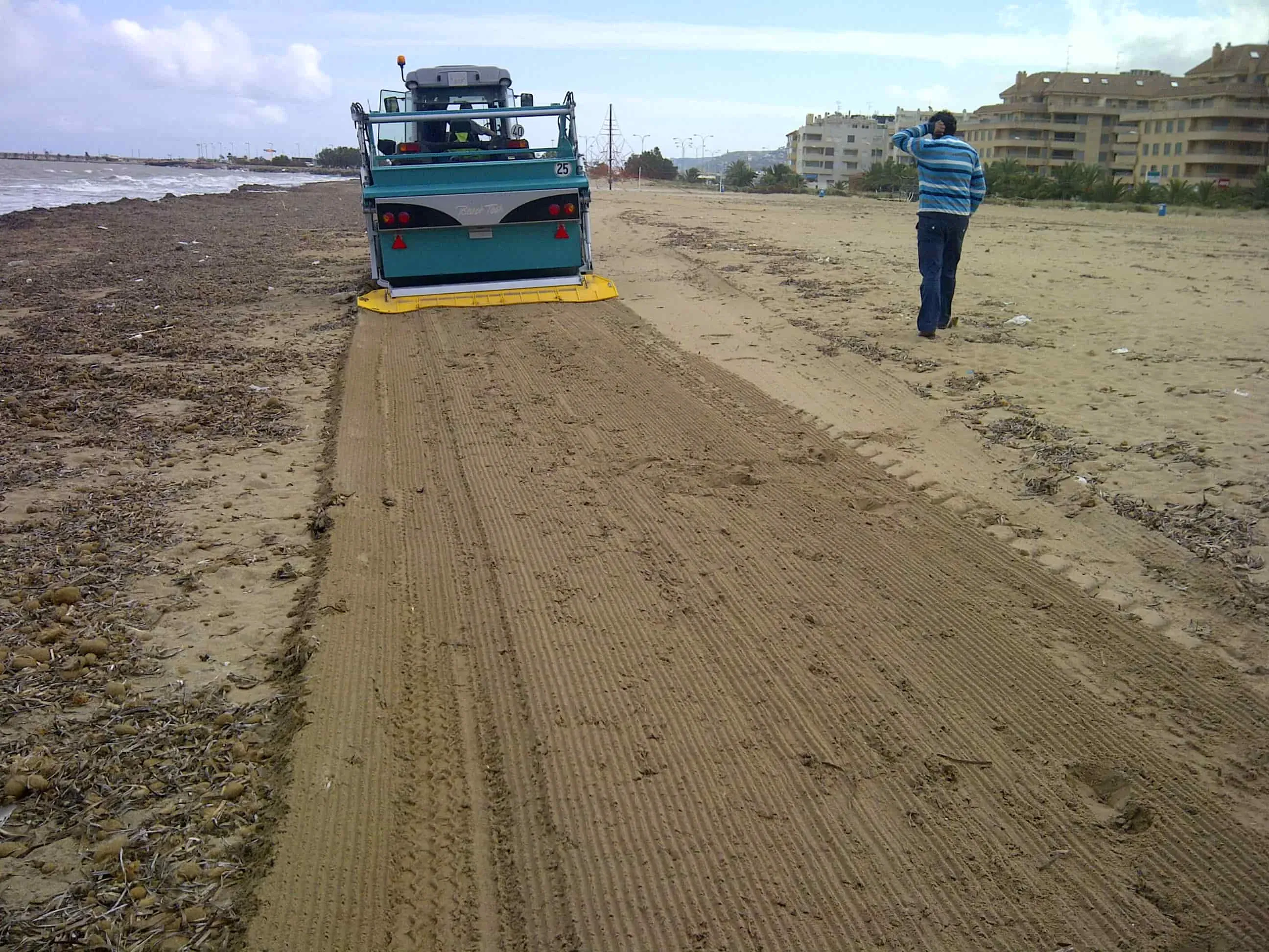 Vue arrière d’une machine BeachTech retirant des algues échouées sur une plage urbaine.