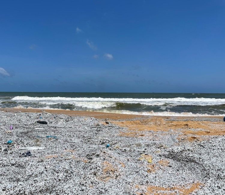 Granuli di resina plastica sparsi lungo la riva sabbiosa – una tipica sfida nella pulizia delle microplastiche.