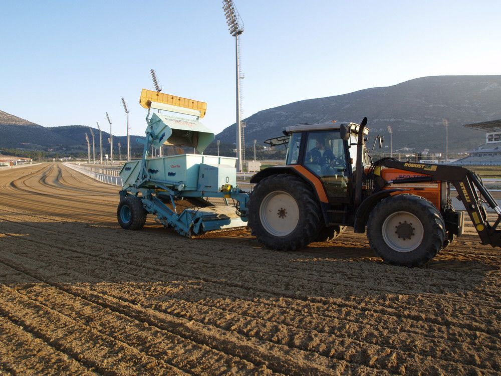 Traktor mit BeachTech Reinigungsmaschine bei der Pflege eines Reitplatzes in einem großen Sportstadion.