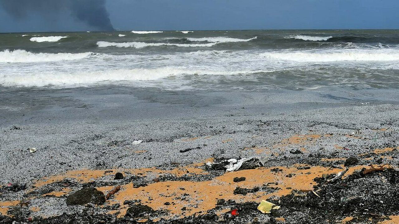 Plastikgranulat (Nurdles) am Strand von Sri Lanka, im Hintergrund schwarzer Qualm