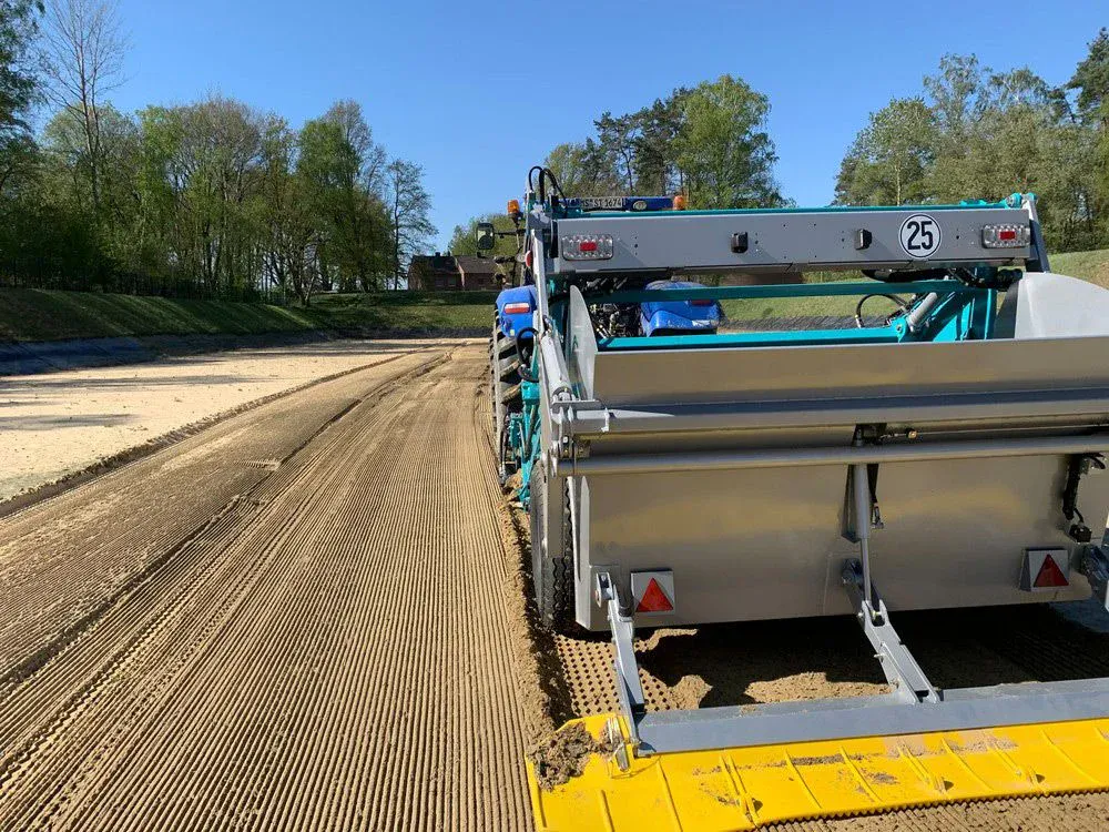 Nahaufnahme von hinten auf eine BeachTech Maschine, die den Sandboden eines Wasserfilterbeckens reinigt, mit klaren Sieblinien im Sand.