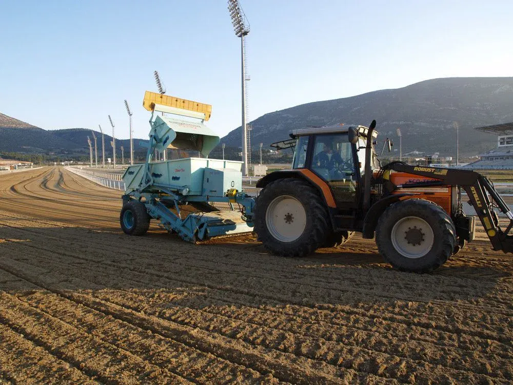 Traktor mit BeachTech Reinigungsmaschine bei der Pflege eines Reitplatzes in einem großen Sportstadion.