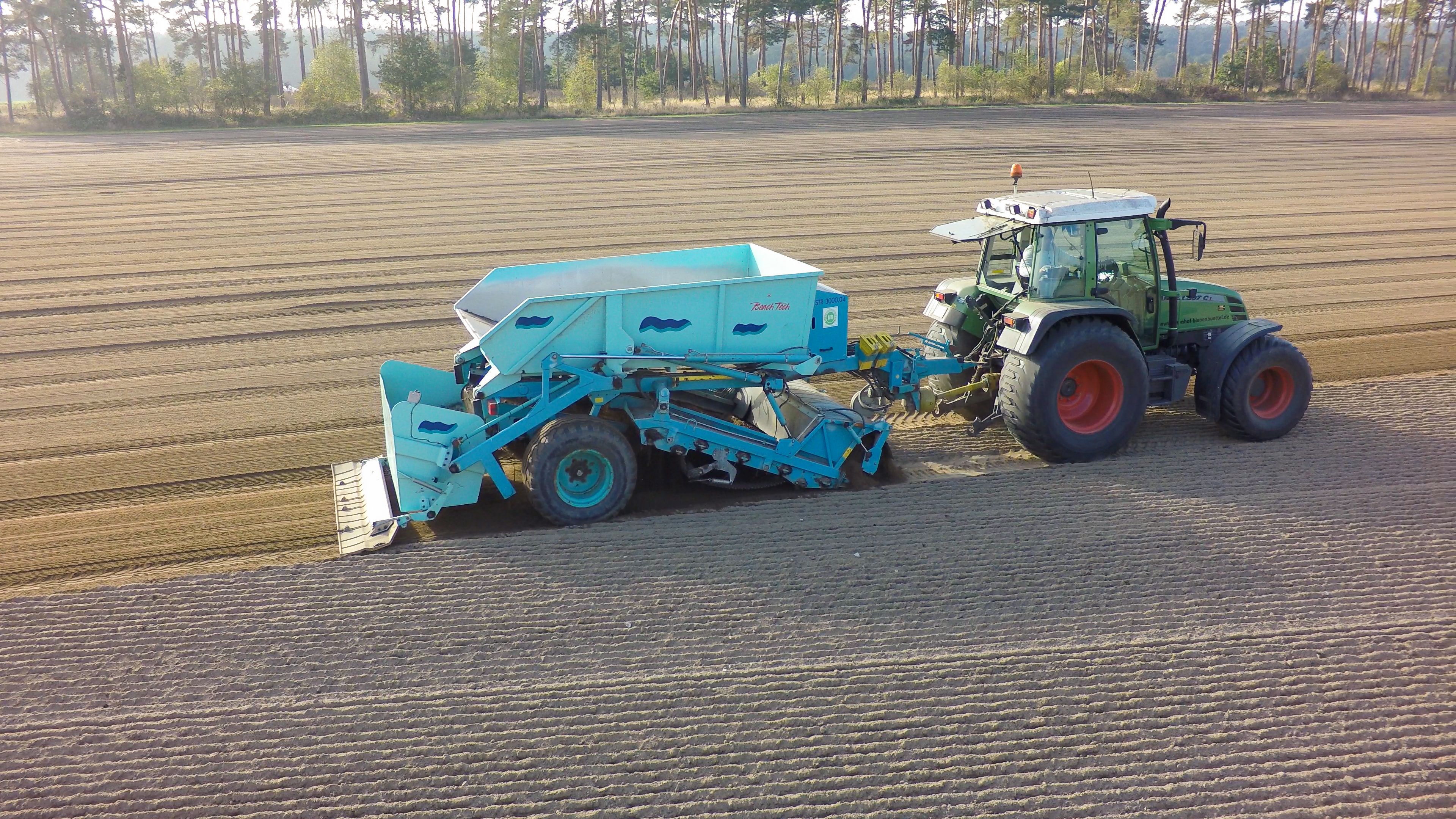 Traktor-gezogener BeachTech Strandreiniger arbeitet auf großer Ackerfläche zur Rollrasen-Produktion