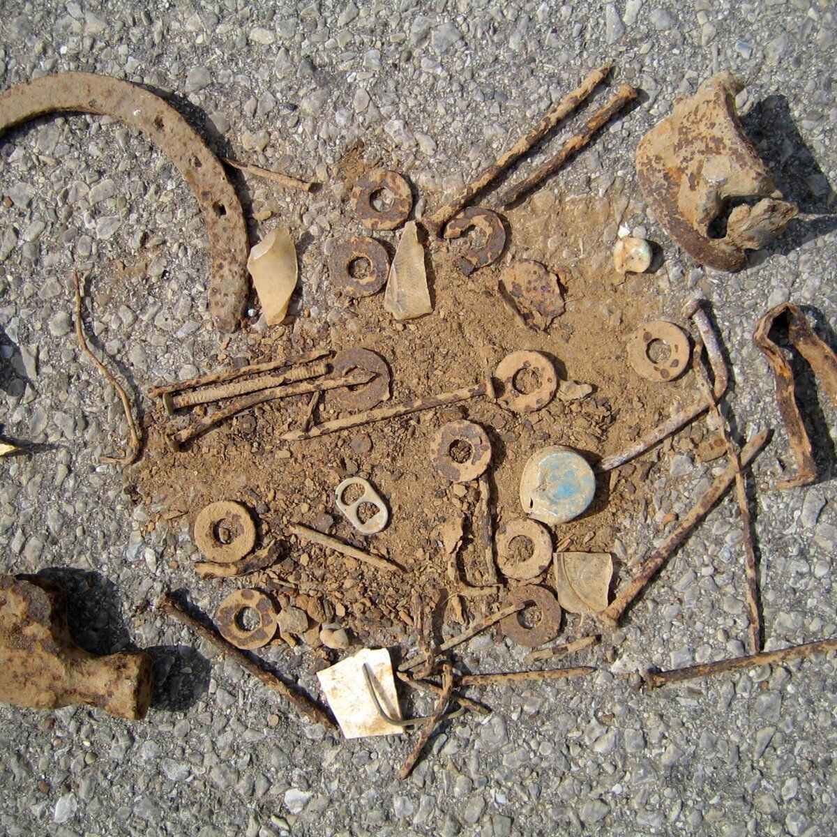 Rostige Metallteile und Nägel im Sand, die eine Verletzungsgefahr darstellen.