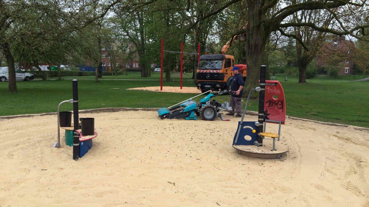 Handgeführter BeachTech Reiniger bei der Säuberung einer kleinen Sandfläche auf einem Spielplatz.